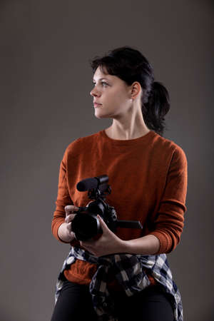 Young female photographer holding a camera in a studio.  She is posed and lit so the background can be changed for composites.  Shot on grey backgroundの写真素材