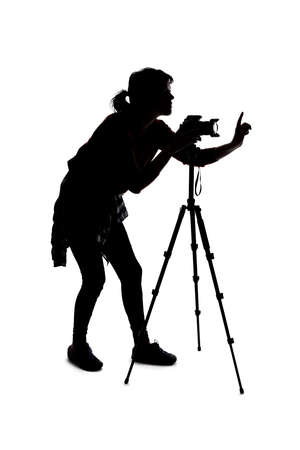 Backlit silhouette of a female photographer hiking and isolated on a white background for composites.  She is holding a camera and posing as a journalist or a hobbyistの写真素材