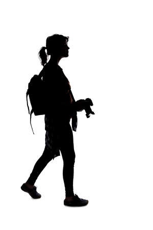 Backlit silhouette of a female photographer hiking and isolated on a white background for composites.  She is holding a camera and posing as a journalist or a hobbyistの写真素材