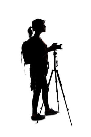 Backlit silhouette of a female photographer hiking and isolated on a white background for composites.  She is holding a camera and posing as a journalist or a hobbyistの写真素材