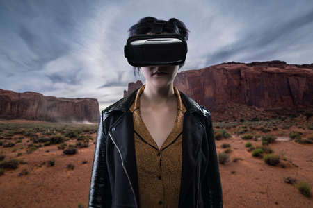 Woman wearing a virtual reality headset in a simulated hiking experience through the desert.  VR tourism is a digital outdoor simulation while staying at homeの写真素材