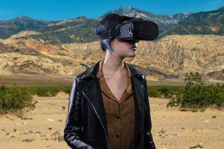 Woman wearing a virtual reality headset in a simulated hiking experience through the desert.  VR tourism is a digital outdoor simulation while staying at homeの写真素材