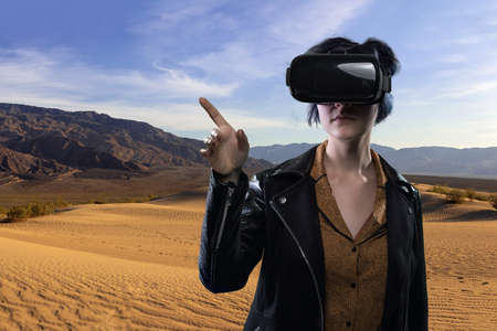 Woman wearing a virtual reality headset in a simulated hiking experience through the desert.  VR tourism is a digital outdoor simulation while staying at homeの写真素材