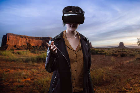 Woman wearing a virtual reality headset in a simulated hiking experience through the desert.  VR tourism is a digital outdoor simulation while staying at homeの写真素材