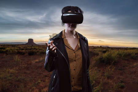 Woman wearing a virtual reality headset in a simulated hiking experience through the desert.  VR tourism is a digital outdoor simulation while staying at homeの写真素材