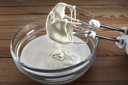 Mixing white cream in bowl with motor mixer. A whisk with a flowing down cream
