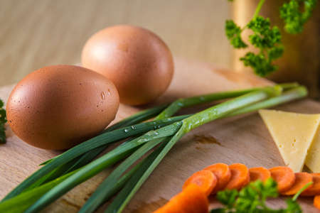 Two raw eggs on the table. Sliced carrots, garlic leaves and cheese. Healthy eating.