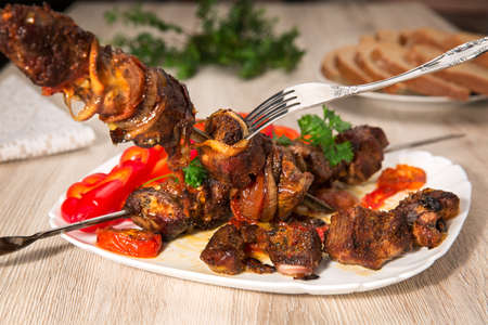Kebabs on skewers. Roasted meat, tomatoes, pepper, parsley and onion on the white dish on the wooden table.の写真素材