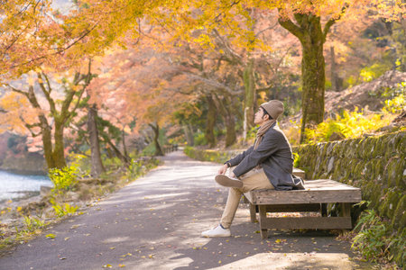 Young man sitting on bench and looking at autumn leaves in Japanの写真素材