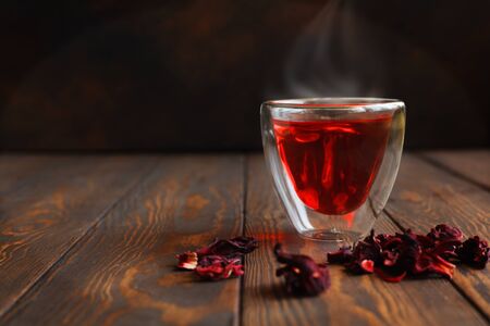 Transparent glass cup with hot hibiscus tea with dry tea leaves on a brown background.の写真素材