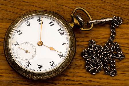 An antique pocket silver watch with a chain on a background of a brown wooden board.の写真素材