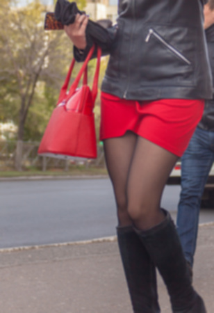 Ablurry slender girl in a red mini skirt, carrying a red bag, walks down the street towards a strong wind.の写真素材