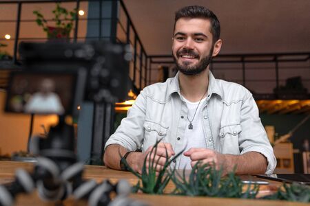 Young man looking at camera while talking to his subscribers. Young blogger with his camera on his...