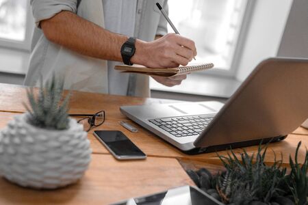 Writing notifications in notepad with laptop and smartphone on work tableの写真素材