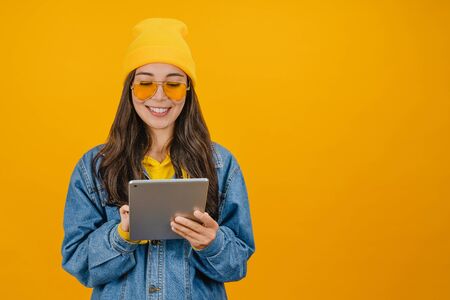Smiling young woman using tablet computer isolated on yellow backgroundの写真素材
