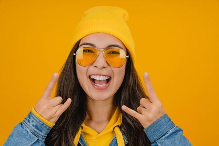 Close up portrait of young woman over isolated yellow background making rock gesture