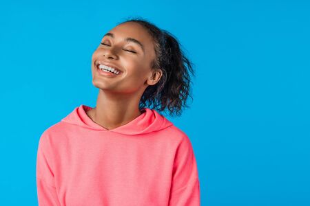 Satisfied african american pleased young female with curly hair isolated on blue studio backgroundの写真素材