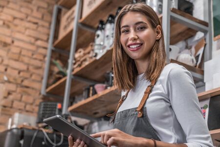 Portrait of a smiling coffee shop owner standing inside her shop and using digital tablet