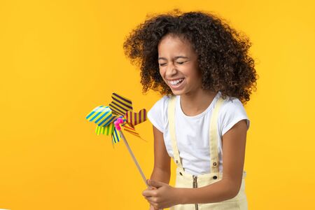 Little girl laughing holding toy windmill isolated on yellow background
