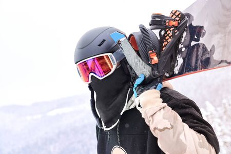 Close up shot of man snowboarder that holding snowboard on his shoulders while looking away with...