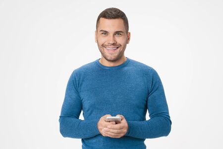 Portrait of smiling young man holding mobile phone isolated over white backgroundの写真素材