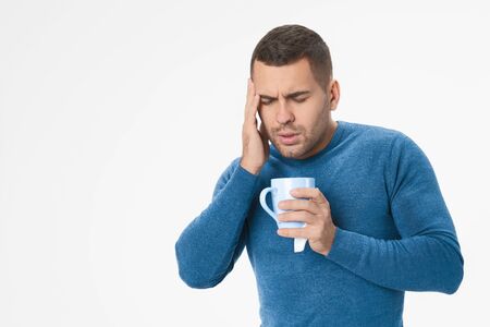 Sick man holding his head with a mug over white backgroundの写真素材