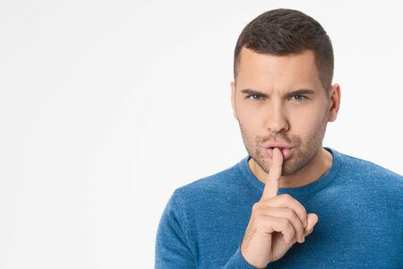 Close up of young man showing silence gesture standing isolated over white background