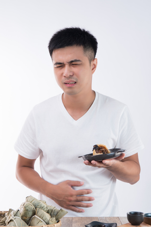 A man has a stomachache after eating delicious zongzi(rice dumpling) on ??Dragon Boat Festival, Asian traditional food, white backgroundの写真素材