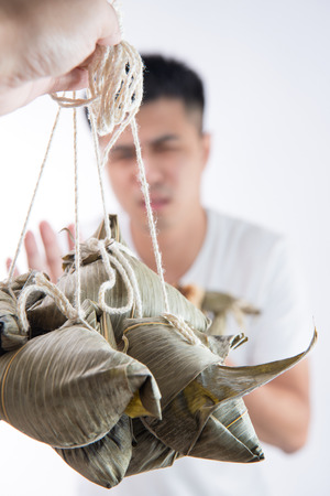A man feels sick after eating too much delicious zongzi(rice dumpling) and saying never eat again on Dragon Boat Festival, Asian traditional food, white backgroundの写真素材