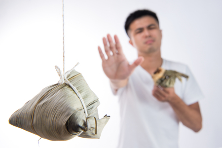 A man feels sick after eating too much delicious zongzi(rice dumpling) and saying never eat again on Dragon Boat Festival, Asian traditional food, white backgroundの写真素材