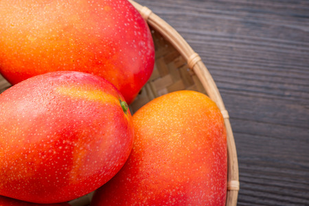 Fresh and beautiful mango fruit in a bamboo basket on a dark wooden background, copy space(text space), blank for text, top view.の写真素材