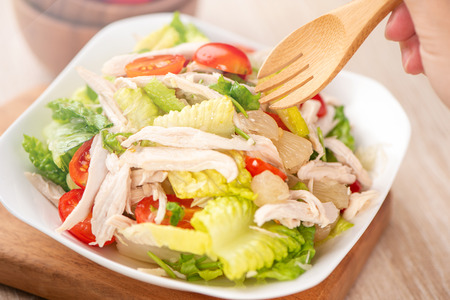 Fresh and delicious homemade chicken salad with tomatoes and pomelos in wooden background, concept of healthy and diet, top view, copy spaceの写真素材