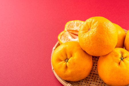 Beautiful and delicous tangerine isolated on red background with bamboo sieve, new modern auspicious and jubilant concept of chinese new year, close up, copy spaceの写真素材