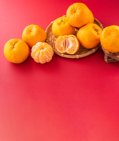 Beautiful and delicous tangerine isolated on red background with bamboo sieve, new modern auspicious and jubilant concept of chinese new year, close up, copy spaceの写真素材