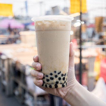 A young woman is holding a plastic cup of brown sugar bubble milk tea at a night market in Taiwan,...
