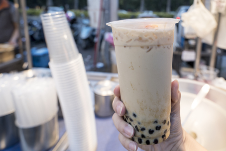 A young woman is holding a plastic cup of brown sugar bubble milk tea at a night market in Taiwan, Taiwan delicacy, close up.の写真素材