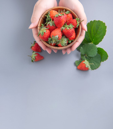 A young woman is holding a bowl of strawberries isolated on a airy blue background, closeup, topview, copyspace.の写真素材