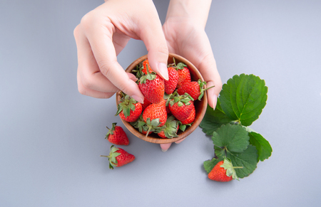 A young woman is holding a bowl of strawberries isolated on a airy blue background, closeup, topview, copyspace.の写真素材