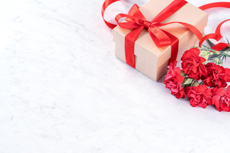 May mothers day concept handmade giftbox idea wishes photography - Beautiful blooming carnations with red ribbon bow box isolated on modern marble desk, close up, copy space, mock upの写真素材