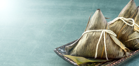 Close up, copy space, famous chinese food in dragon boat (duan wu) festival, steamed rice dumplings pyramidal shaped wrapped by bamboo leaves made by sticky rice raw ingredientsの写真素材