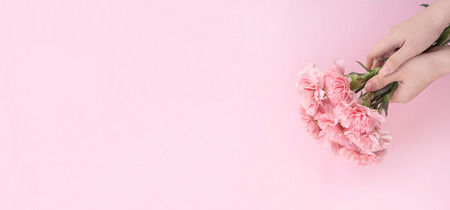 Woman giving bunch of elegance blooming baby pink color tender carnations isolated on pale pink background, mothers day decor design concept, top view, close up, copy spaceの写真素材