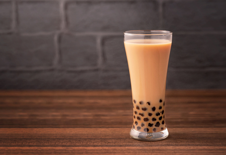 Delicious bubble milk tea with tapioca pearl ball in glass on wooden table and dark gray brick background, popular food and drink in Taiwan, close upの写真素材