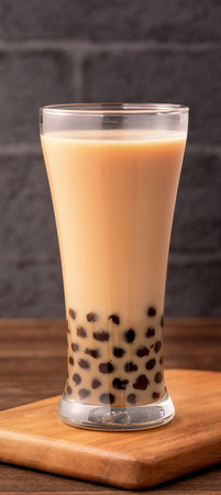 Delicious bubble milk tea with tapioca pearl ball in glass on wooden table and dark gray brick background, popular food and drink in Taiwan, close upの写真素材