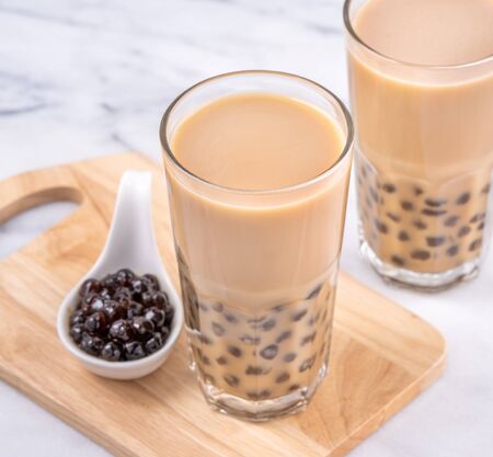 Popular Taiwan drink - Bubble milk tea with tapioca pearl ball in drinking glass on marble white table wooden tray background, close up, copy spaceの写真素材