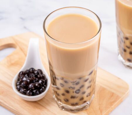 Popular Taiwan drink - Bubble milk tea with tapioca pearl ball in drinking glass on marble white table wooden tray background, close up, copy spaceの写真素材