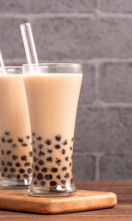 Popular Taiwan drink - Bubble milk tea with tapioca pearl ball in drinking glass and straw, wooden table gray brick background, close up, copy spaceの写真素材