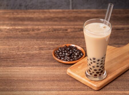 Popular Taiwan drink - Bubble milk tea with tapioca pearl ball in drinking glass and straw, wooden table gray brick background, close up, copy spaceの写真素材