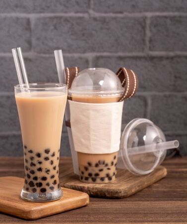 Takeout with disposable item concept popular Taiwan drink bubble milk tea with plastic cup and straw on wooden table background, close up, copy spaceの写真素材