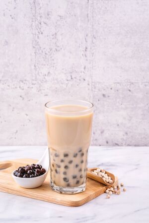 Popular Taiwan drink - Bubble milk tea with tapioca pearl ball in drinking glass on marble white table wooden tray background, close up, copy spaceの写真素材