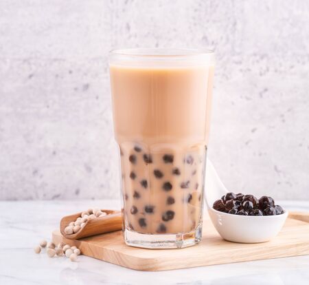 Popular Taiwanese tea-based drink - Bubble milk tea on wooden tray on white marble tableの写真素材